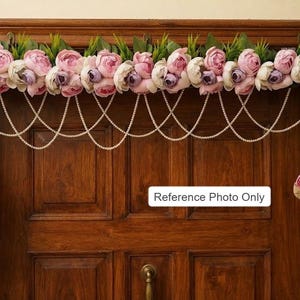May include: A door hanging decoration featuring a horizontal arrangement of pink and white artificial peonies with green leaves, accented by multiple draped strands of white pearls and two vertical floral clusters. Text reads: Reference Photo Only.