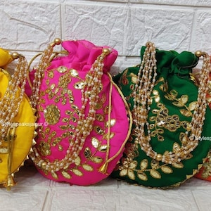 Puede incluir: Cuatro coloridas bolsas con cordón en amarillo, rosa, verde y naranja. Cada bolsa está adornada con bordados dorados y una correa de cuentas. Las bolsas están dispuestas en fila, mostrando sus colores vibrantes y detalles intrincados.