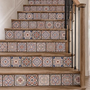 Op de afbeelding: Een houten trap met decoratieve tegelstickers op elke stootbord. De stickers tonen een herhalend patroon van geometrische en florale motieven in blauw-, rood- en crèmetinten, wat een contrast vormt met de treden van natuurlijk hout.