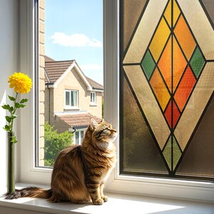 Puede incluir: Un gato atigrado marr&oacute;n y esponjoso est&aacute; sentado en un alf&eacute;izar blanco, mirando hacia arriba. Una flor amarilla en un jarr&oacute;n verde est&aacute; a la izquierda. Una vidriera con formas geom&eacute;tricas en naranja, amarillo, verde y rojo est&aacute; a la derecha. Se ve una casa.