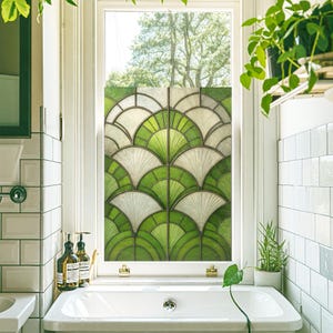 Könnte beinhalten: Ein Fenster mit einer dekorativen Folie mit einem fächerförmigen Design in Grün- und Weißtönen. Das Fenster befindet sich in einem Badezimmer, mit einem weißen Waschbecken, Seifenflaschen und Pflanzen. Das Design verleiht einen Hauch von Eleganz und Privatsphäre.