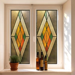 Puede incluir: Una ventana con dos paneles con dise&ntilde;os de vidrieras. El vidrio tiene un patr&oacute;n de diamantes con colores naranja, amarillo, verde y blanco. Tres botellas de vino y una planta en maceta est&aacute;n en el alf&eacute;izar.