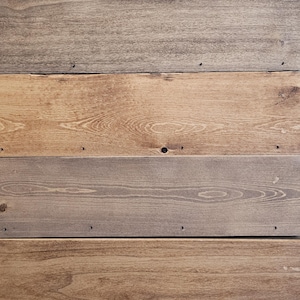 Puede incluir: Primer plano de una superficie de madera compuesta por tablas horizontales. Las tablas var&iacute;an en color, desde marr&oacute;n claro hasta gris. La veta de la madera es visible y hay peque&ntilde;os agujeros de clavos.