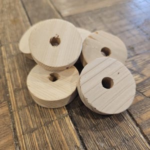 May include: A collection of unfinished wooden wheels with a central hole. The wheels are light-colored and appear to be made of softwood. The wood grain is visible on the surface of the wheels. The wheels are likely for a craft project or toy.