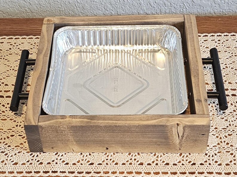 Puede incluir: Una bandeja de madera con una bandeja rectangular de papel de aluminio. La bandeja es de madera marr&oacute;n claro y tiene asas de metal negro a cada lado. La bandeja de aluminio est&aacute; vac&iacute;a y tiene un patr&oacute;n de diamantes en la parte inferior.