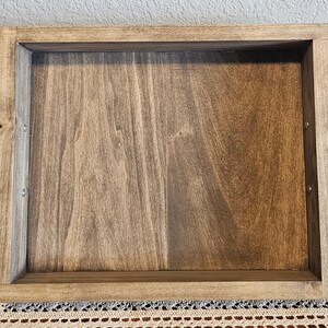 Puede incluir: Una bandeja de madera rectangular con acabado te&ntilde;ido. La bandeja tiene un borde elevado y asas de metal negro en cada extremo. La veta de la madera es visible.