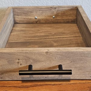 Puede incluir: Una bandeja rectangular de madera con tinte oscuro y asa negra. La bandeja es de madera y tiene un dise&ntilde;o sencillo y moderno. La bandeja es perfecta para servir alimentos o exhibir objetos.