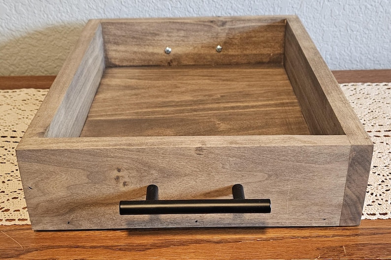 Puede incluir: Una bandeja rectangular de madera con tinte oscuro y asa negra. La bandeja es de madera y tiene un dise&ntilde;o sencillo y moderno. La bandeja es perfecta para servir alimentos o exhibir objetos.