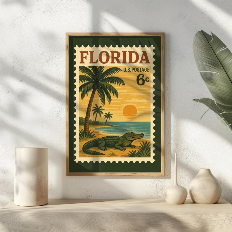 May include: Framed vintage-style Florida postage stamp art print. The artwork features a beach scene with palm trees, an alligator, and a sunset. The stamp reads "Florida" and "U.S. Postage 6c". The frame is a dark green color.