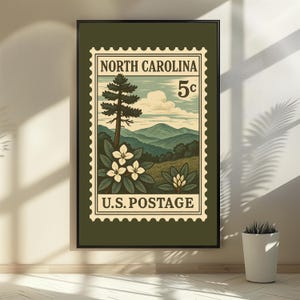 May include: A framed wall art print featuring a vintage-style postage stamp design. The graphic depicts a North Carolina landscape with mountains, a tall pine tree, and white rhododendron flowers. Text reads NORTH CAROLINA 5c U.S. POSTAGE.