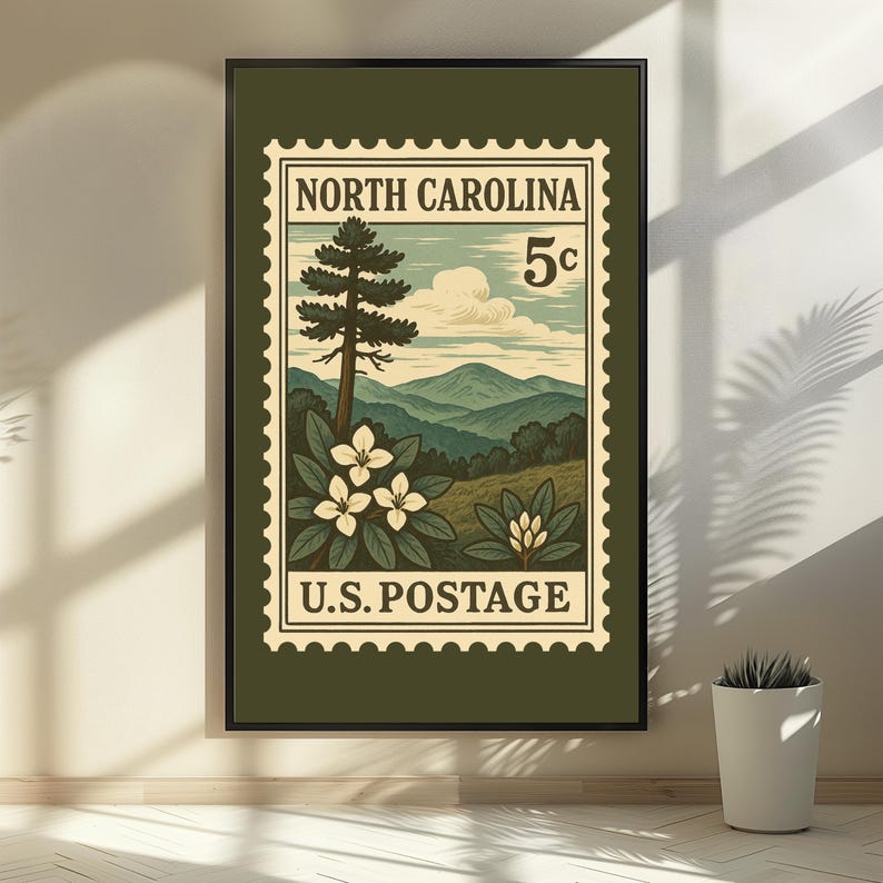 May include: A framed wall art print featuring a vintage-style postage stamp design. The graphic depicts a North Carolina landscape with mountains, a tall pine tree, and white rhododendron flowers. Text reads NORTH CAROLINA 5c U.S. POSTAGE.