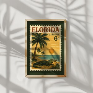 May include: Framed vintage Florida postage stamp art. The stamp features a beach scene with palm trees, an alligator, and a setting sun. The text "Florida" and "U.S. Postage 6c" are printed at the top. The frame is a dark green color.