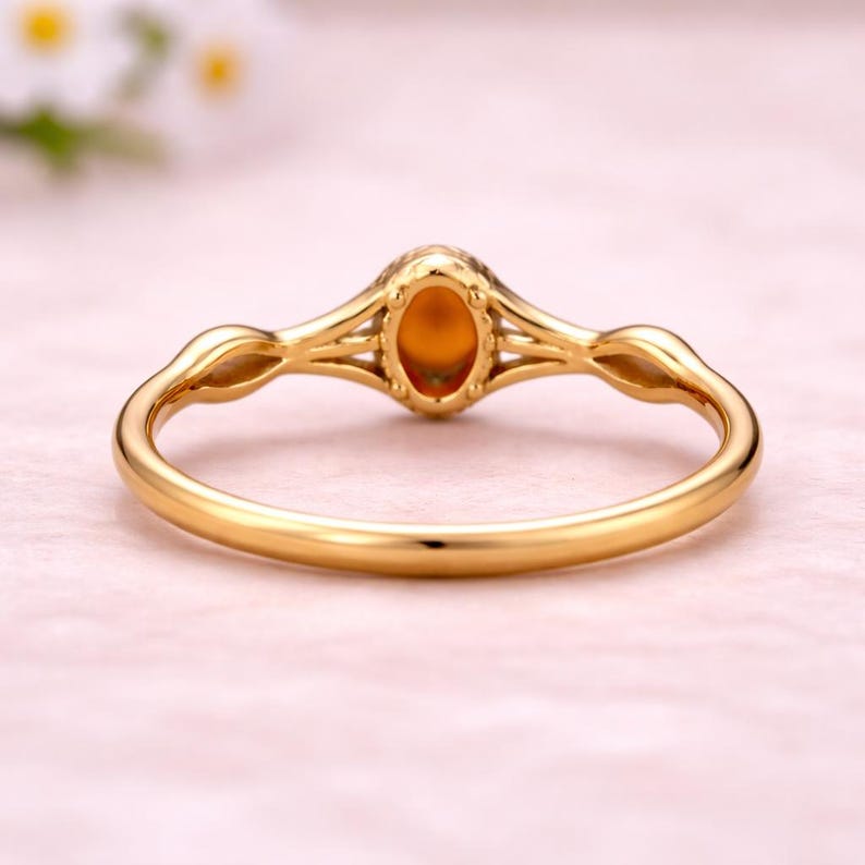 May include: A gold ring with an oval, amber-colored gemstone. The ring has a delicate, openwork design with a slender band and decorative accents on the shoulders. The gemstone is set in a bezel setting.