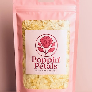 May include: A pink pouch filled with dried yellow rose petals. The pouch has a label with a red rose logo and the text "Poppin' Petals Dried Rose Petals". The background is a solid pink.