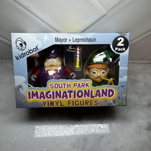 May include: A Kidrobot two-pack of South Park Imaginationland vinyl figures. The box features Mayor and Leprechaun characters. The box has the text "Mayor + Leprechaun" and "2 Pack". The box also has the text "South Park Imaginationland Vinyl Figures".