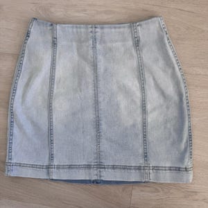 May include: Pale blue denim skirt with a classic design. The skirt has vertical seams and a zip closure. The fabric has a faded wash, giving it a vintage look. The skirt is a mini length.