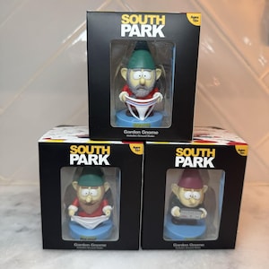 May include: Three boxed South Park Garden Gnome figurines. Each gnome wears a different outfit and hat. The boxes are black with the South Park logo and the words "Garden Gnome". The boxes also have a clear window showing the figurine.