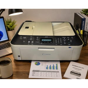 May include: A white Canon PIXMA MX340 all-in-one printer featuring a black control panel with a digital display, numeric keypad, and function buttons. The printer has a top document feeder tray and a front paper output slot, with a printed report nearby.