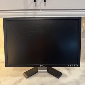 May include: A black Dell computer monitor featuring a rectangular screen with a thin black bezel. The monitor is supported by a silver and black stand with a wide, flat base. The Dell logo is printed in white on the bottom centre of the frame.