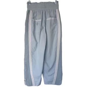 May include: Pale blue athletic trousers with white side stripes and an elasticated waistband. The trousers have two pockets and a small logo near the back pocket. The trousers are hanging on a metal hanger.