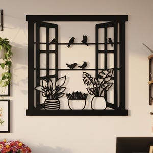Könnte beinhalten: Schwarze Metall-Wandkunst, die ein Fenster mit geöffneten Fensterläden darstellt, mit Silhouetten von Vögeln und Topfpflanzen. Das Kunstwerk ist an einer weißen Wand angebracht, mit gerahmten Blumendrucken und Hängepflanzen. Ein Schild mit der Aufschrift "FRESH BLOOMS" ist sichtbar.