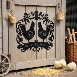 Può includere: Cartello per pollaio in metallo nero con due galli, decorazioni floreali e la scritta "Oliver's Hen House". Il cartello è montato su una porta di legno. Pulcini e mais piccoli in primo piano. Due piccoli cestini di vimini sono appesi.