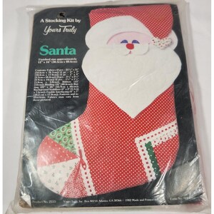 May include: A Christmas stocking kit by Yours Truly, featuring a Santa Claus design. The kit includes fabrics, ribbon, and fusible interfacing. The finished size is approximately 12" x 16" (30.5cm x 40.6cm).
