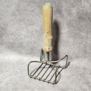 Machacador de patatas antiguo y primitivo, de metal cuadrado con cabezal de alambre y mango de madera.