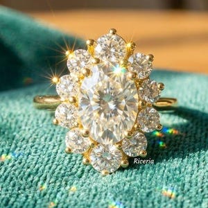 May include: A gold ring with a large, oval-shaped, clear gemstone surrounded by smaller, round gemstones. The ring is set on a teal velvet surface, with the light reflecting off the gemstones.