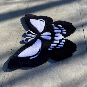 May include: A black and white butterfly-shaped rug. The rug features a black background with white accents outlining the wings and body. The butterfly design is detailed and textured, creating a visually appealing home decor item.