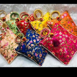 Puede incluir: Una colección de bolsos de mano bordados en varios colores, incluyendo rosa, naranja, amarillo, azul y verde. Cada bolso presenta patrones florales, ribete de cuentas y un asa decorativa. Las borlas y adornos añaden al diseño ornamentado.