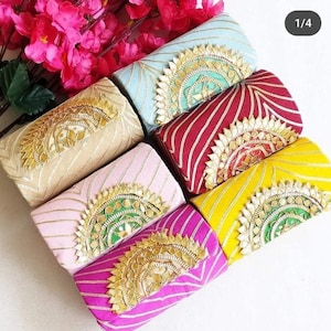 Puede incluir: Una colección de coloridos bolsos de mano decorativos. Cada bolso presenta un color único, como azul claro, rosa, amarillo y rojo. Los bolsos están adornados con adornos dorados y patrones intrincados, creando un diseño lujoso y llamativo.