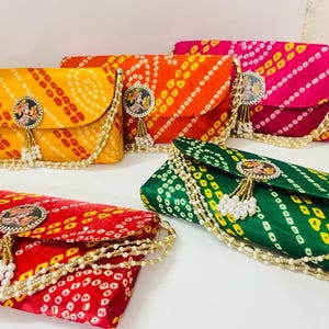 May include: A collection of colorful, patterned clutch purses. The purses are in shades of yellow, orange, red, pink, and green. Each purse has a decorative clasp with a tassel and pearl chain trim. The purses are arranged on a white surface.