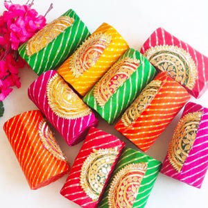 Könnte beinhalten: Eine Sammlung farbenfroher, rechteckiger Clutch-Geldbörsen. Die Geldbörsen weisen Streifenmuster in verschiedenen Farben auf, darunter Grün, Gelb, Rosa, Rot und Orange. Jede Geldbörse hat eine goldfarbene Verzierung.