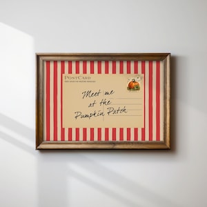 May include: A framed print featuring a vintage-style postcard design with a tan background and red vertical stripes. The postcard displays the text "Meet me at the Pumpkin Patch" in black script, with a small illustration of an orange pumpkin.