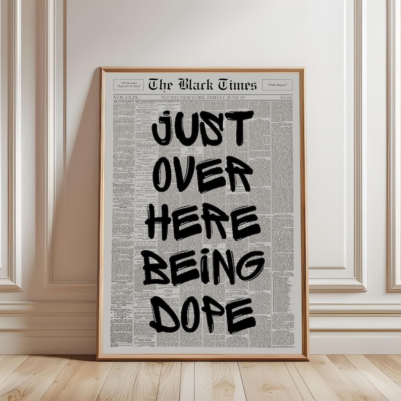 Puede incluir: Una l&aacute;mina de arte mural enmarcada con un fondo de peri&oacute;dico antiguo titulado The Black Times. Superpuesto en grandes letras negras en negrita con trazos de pincel aparece el texto JUST OVER HERE BEING DOPE. Marco de madera clara.