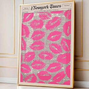 May include: A framed print featuring a collage of bright pink lipstick kiss marks over a vintage newspaper background. The print is in a gold frame and includes the text "The New York Times" at the top. A stylish and unique wall art piece.