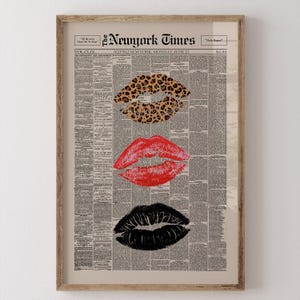 May include: Framed print featuring three sets of lips in leopard print, red, and black, set against a vintage newspaper background. The top of the print displays the text "The New York Times" and the date "Monday, June 21". The print is encased in a wooden frame.
