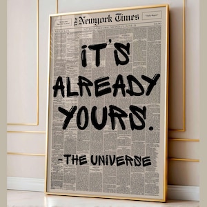 Könnte beinhalten: Gerahmter Druck mit einem Zeitungs-Hintergrund. Der Titel "The New York Times" ist zu sehen. Der schwarze Text lautet "IT'S ALREADY YOURS. - THE UNIVERSE." Der goldene Rahmen verleiht dem Motiv einen edlen Look.