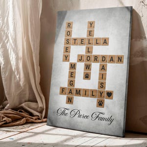 May include: A canvas print with a crossword puzzle design, featuring names and the word "FAMILY" spelled out using wooden letter tiles. Includes paw prints and a heart symbol. The text "The Pierce Family" is written below.