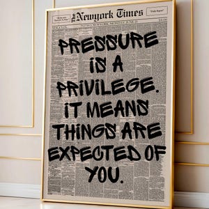 May include: A framed print featuring a vintage newspaper background with the headline "New York Times." Bold black text reads "PRESSURE IS A PRIVILEGE. IT MEANS THINGS ARE EXPECTED OF YOU." The frame is gold.