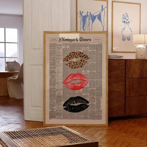 May include: A framed artwork featuring three sets of lips in different styles. The top lip print has a leopard pattern, the middle is red, and the bottom is black. The background is a newspaper print with the words "New York Times" at the top.
