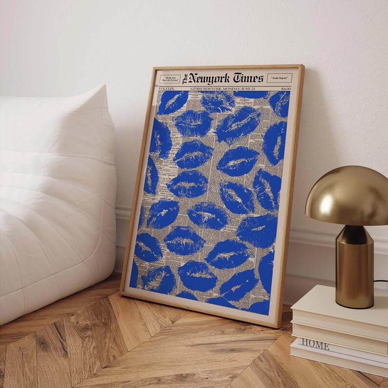 May include: A framed print featuring blue lipstick kiss marks on a newspaper background. The print is in a wooden frame and leans against a wall. The text "New York Times" is visible at the top of the print.