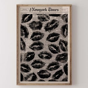 May include: A framed print featuring a collage of black lipstick kiss marks over a vintage newspaper background. The newspaper is from The New York Times, dated June 21. The print is in a wooden frame.