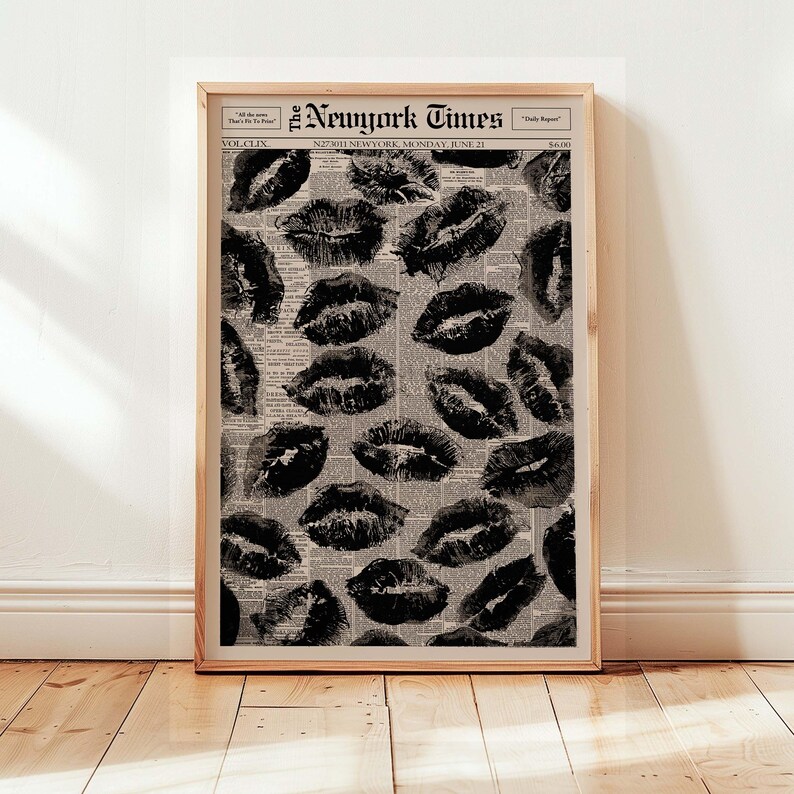 May include: A framed print featuring a pattern of black lipstick kiss marks over a vintage newspaper background. The newspaper headline reads "The New York Times" with the date "Monday, June 21". The print is displayed in a wooden frame.