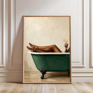 Könnte beinhalten: Gerahmtes Kunstwerk, das eine Person zeigt, die sich in einer dunkelgrünen Badewanne mit Löwenfüßen entspannt. Die Beine der Person sind sichtbar, und sie hält einen Cocktail mit einer Zitronenscheibe. Der Hintergrund ist eine strukturierte, cremefarbene Wand.