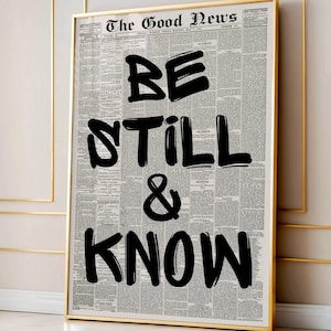 May include: A framed print with a newspaper background and the words "BE STILL & KNOW" in bold, black lettering. The print is in a gold frame. The artwork conveys a message of peace and reflection, suitable for home decor.