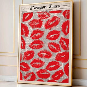 May include: A framed print featuring a collage of red lipstick kiss marks over a vintage newspaper background. The newspaper is titled "The New York Times" with the date "Monday, June 21". The print is in a gold frame.