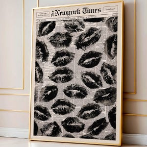 May include: A framed print featuring a collage of black lipstick kiss marks over a vintage newspaper background. The newspaper is titled "The New York Times" with the date "Monday, June 21". The print is encased in a gold frame.