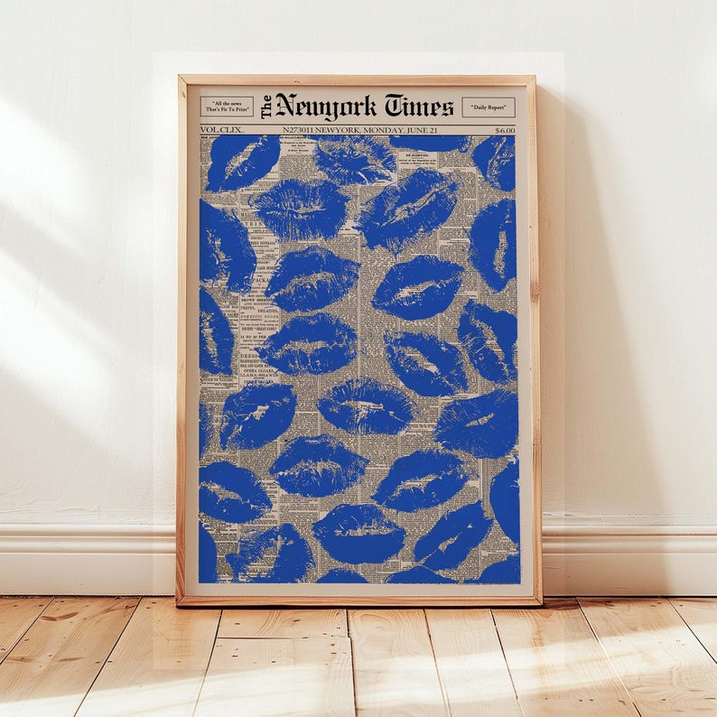 May include: A framed print featuring a collage of blue lipstick prints over a vintage newspaper background. The newspaper is from The New York Times, dated Monday, June 21. The print is displayed on a wooden floor.